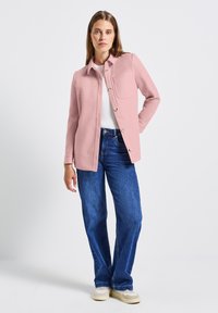Růžová košile s límečkem a knoflíky, s přední kapsou, kombinovaná s modrými širokými džíny a béžovými teniskami. Hladká textura.