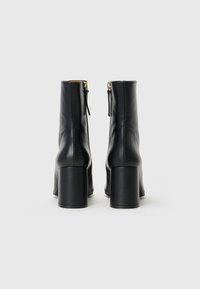 Black leather ankle boots with a smooth texture, high block heels, and gold zipper details at the back, featuring a sleek, fitted design.