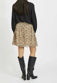 Svart långärmad topp, kjol i tan och bruna mönster, knähöga svarta läderstövlar med blockklackar, slät struktur, flödande silhuett.