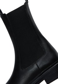 Stivale in pelle nera con pannelli laterali elasticizzati, dalla texture liscia e con punta tondeggiante. Presenta un tacco basso a blocco e righe orizzontali sulla suola.