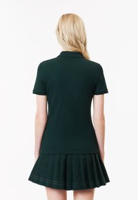 Polo shirt verde scuro con maniche corte, caratterizzato da colletto a costine e un design a gonna plissettata in tessuto abbinato nella parte inferiore.