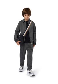 Giacca grigia con zip e pantaloni abbinati dal taglio sartoriale, maglietta nera sotto, sneakers bianche e una borsa a tracolla con una tracolla a righe.