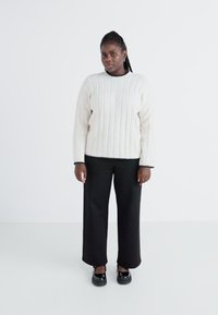 Cream ribbed sweater with a high neckline and black trim, paired with black wide-leg trousers and black shoes. Smooth texture.