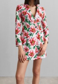 Robe blazer florale en rose et blanc, dotée d'un décolleté en V profond, de manches longues et d'une silhouette cintrée avec des accents de feuilles vertes.
