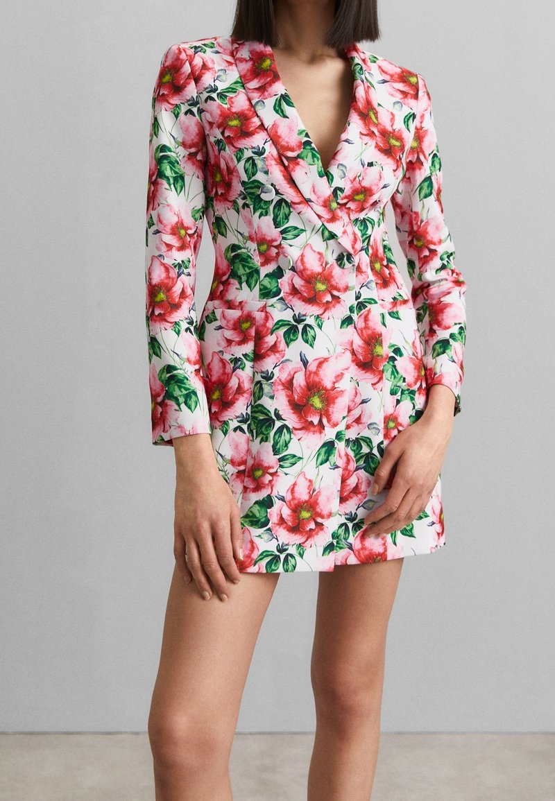Robe blazer florale en rose et blanc, dotée d'un décolleté en V profond, de manches longues et d'une silhouette cintrée avec des accents de feuilles vertes.