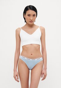 Hvit kort bralette med tynne stropper og V-hals, sammen med lyseblå bikini-truser med en hvit kant med logo.