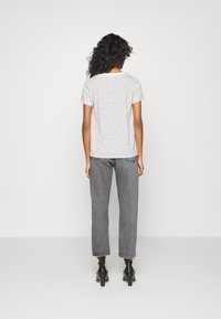 Camiseta blanca con pequeños lunares negros, de manga corta y cuello redondo, combinada con pantalones vaqueros grises de talle alto y botas negras de tacón.
