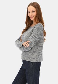 Szary sweter dziany o teksturowanym wykończeniu, z okrągłym dekoltem i długimi rękawami, w zestawie z ciemnymi dżinsami.