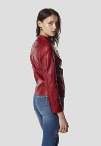 Červená kožená bunda s priliehavým dizajnom, textúrovaným povrchom a viditeľným prešitím. Kombinovaná s modrými rifľami s vyšívanými detailmi.