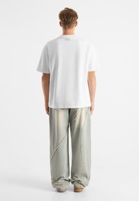 Vit bomullströja med rund halsringning, kombinerad med oversized ljusgrå jeans med kontrasterande sömmar och en avslappnad passform.