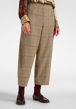 Beige geruite wijde broek met hoge taille, gecombineerd met bordeaux sokken en donkerbruine loafers, gedragen met een blouse met lange mouwen en patroon.