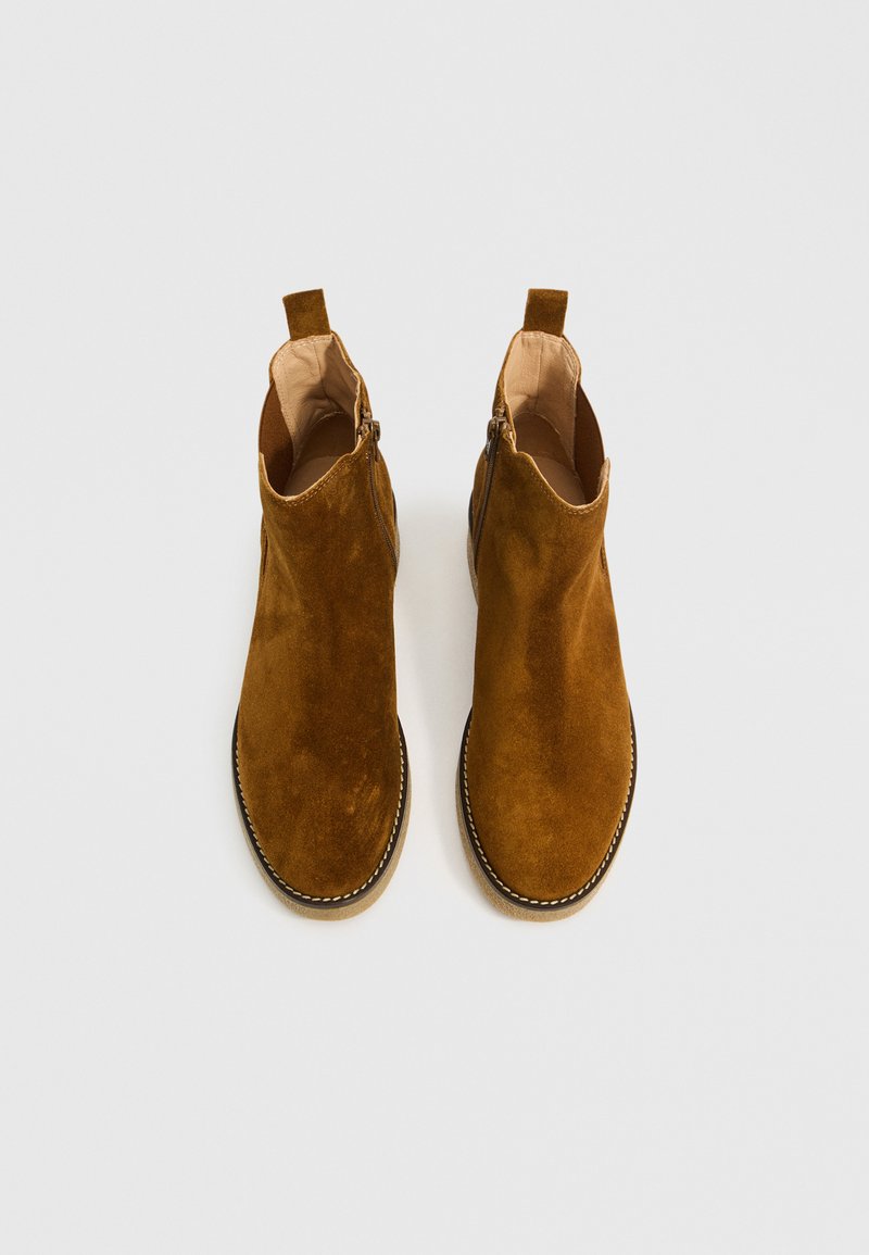 Brązowe zamszowe botki za kostkę z zamkiem błyskawicznym z boku, okrągłym noskiem i kontrastowym haftem wzdłuż podeszwy. Miękka tekstura i minimalistyczny design.