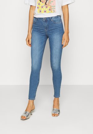 Jeans de denim azul ajustados con cintura alta, que presentan un ligero desvanecimiento y un clásico diseño de cinco bolsillos. Combinados con tacones abiertos plateados.