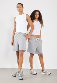 Shorts en coton gris avec poches et taille à cordon de serrage, assortis à des tops sans manches blancs. Tous deux portent des chaussures de sport.