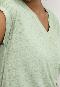 T-shirt verde chiaro con scollo a V e maniche corte, caratterizzato da un tessuto testurizzato e una vestibilità rilassata. Nessun motivo o accento visibile.