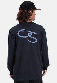 Navy long-sleeve t-shirt featuring a light blue snake graphic on the back. Made of cotton with a relaxed fit and round neckline.