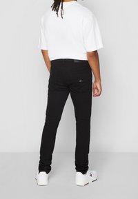 Vaqueros de mezclilla negra con corte ajustado, que presentan bolsillos traseros y una etiqueta de cuero en la cintura. Combinados con una camiseta blanca y zapatillas blancas.