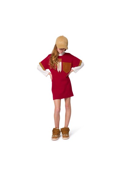 Rode jurk met korte mouwen en een bruine voorzak, gelaagd over een witte blouse met lange mouwen, gecombineerd met bruine en panterprint hoge sneakers.