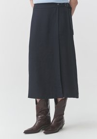 Gonna blu navy realizzata in tessuto liscio, con una tasca laterale e dettagli di chiusura, abbinata a stivali cowboy in pelle marrone.
