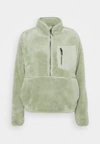 Sudadera de forro polar verde con cuello alto, media cremallera en la parte delantera y un bolsillo en el pecho. Textura suave y ajuste relajado. Presenta una cremallera de contraste.