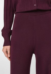 Haut en maille bordeaux avec texture côtelée et détail de boutons, associé à un pantalon ajusté assorti en tissu lisse, mettant en valeur un design cohérent.