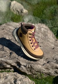 Botas de senderismo impermeables de color marrón con acentos en marrón, cuello acolchado y cordones burdeos. Suela ligera y superficie texturizada para mayor agarre.
