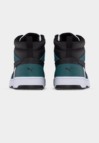 Ζευγάρι πράσινων και μαύρων ψηλών αθλητικών παπουτσιών με λευκές σόλες, εμφανιζόμενα από πίσω σε απλό λευκό φόντο.