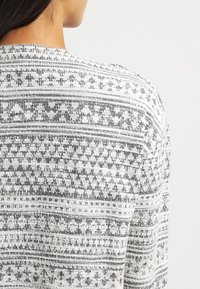 Svartvit mönstrad tröja med intrikata geometriska mönster, en löst stickad textur och rundad halsringning.