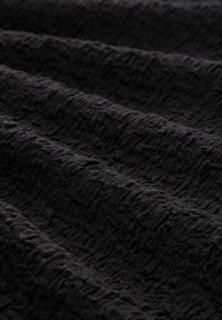 Černá texturovaná tkanina s vrásčitou povrchovou strukturou; měkký, tkaný materiál zdůrazňuje hloubku a vzor svými nerovnoměrnými výstupky.