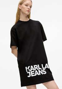Prevelika crna majica haljina od pamuka s kratkim rukavima. Sadrži bijeli natpis "KARL LAGERFELD JEANS" na rubu. Jednostavan, ležeran dizajn.