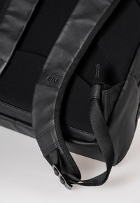Zaino nero con una finitura opaca e liscia, dotato di spallacci in tessuto imbottito e una tasca laterale. Materiali resistenti e design minimalista.