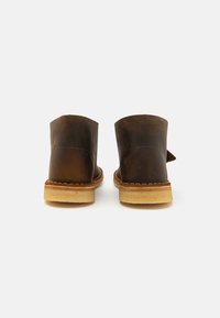 Braune Leder-Stiefeletten mit runden Spitzen und einer kontrastierenden beigen Sohle, die sichtbare Nähte und einen leichten Absatz aufweisen.