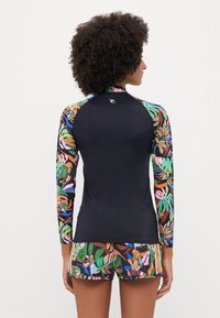 Rash guard su juodu nugariniu, spalvingomis gėlėtomis rankovėmis ir suderintais raštuotais šortais. Pagamintas iš tamprios medžiagos, užtikrinančios komfortą ir judrumą.