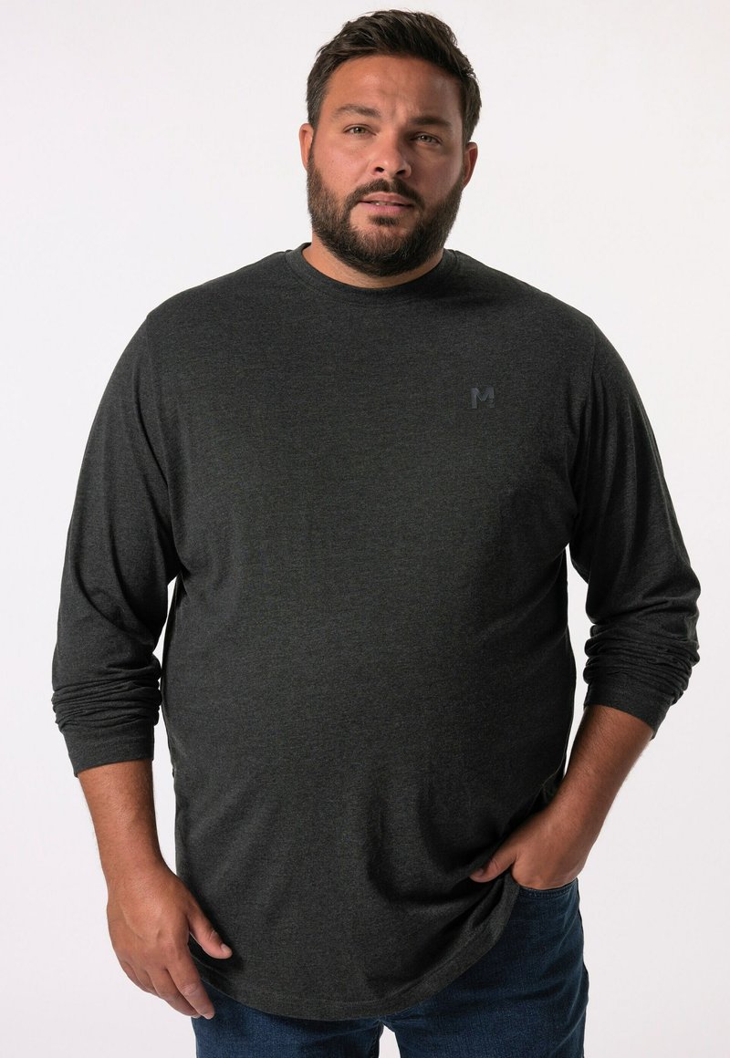 Langärmliges, dunkelgraues T-Shirt aus weichem Material mit abgerundetem Saum und subtiler Logo auf der linken Brust. Kombiniert mit blauen Jeans.