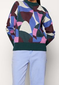 Monivärinen villapaita, jossa on abstrakteja muotoja sinisessä, vaaleanpunaisessa, burgundinpunaisessa ja vihreässä. Raitakuvioinen kaulus ja helma, teksturoitu neulottu kangas.