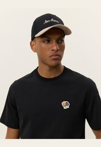 Black short-sleeve t-shirt with a round neckline and an embroidered floral patch in orange, purple, and green on the left chest.