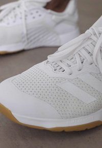 Witte sportieve schoenen van meshmateriaal, met een rubberen zool en twee opvallende witte strepen aan de zijkant. Kenmerken zijn onder andere veters en gestructureerde panelen.