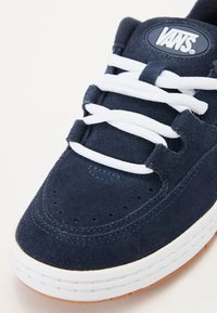 Marineblå semsket sneakers med hvite lisser, rund tå, perforerte detaljer, og en hvit gummisåle med en gummiyttersåle.