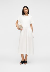 Λευκό μίντι φόρεμα με κοντά μανίκια, απαλή υφή, εφαρμοστή μέση και φαρδύ φούστα. Το μοντέλο το συνδύασε με μαύρες σαγιονάρες και μπεζ τσάντα χειρός.