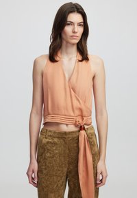 Top halter pesca con design avvolgente e nodo anteriore. Pantaloni marroni testurizzati con dettaglio di cintura laterale. Entrambi hanno una vestibilità comoda.