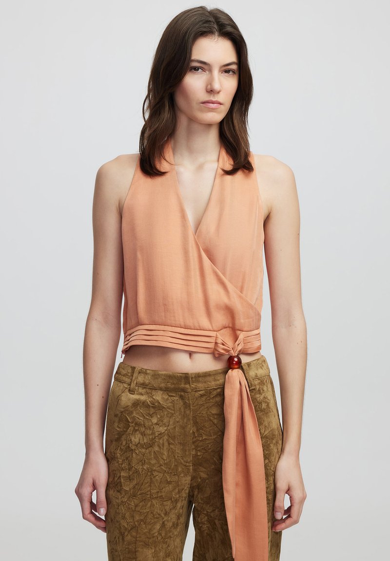 Top halter pesca con design avvolgente e nodo anteriore. Pantaloni marroni testurizzati con dettaglio di cintura laterale. Entrambi hanno una vestibilità comoda.