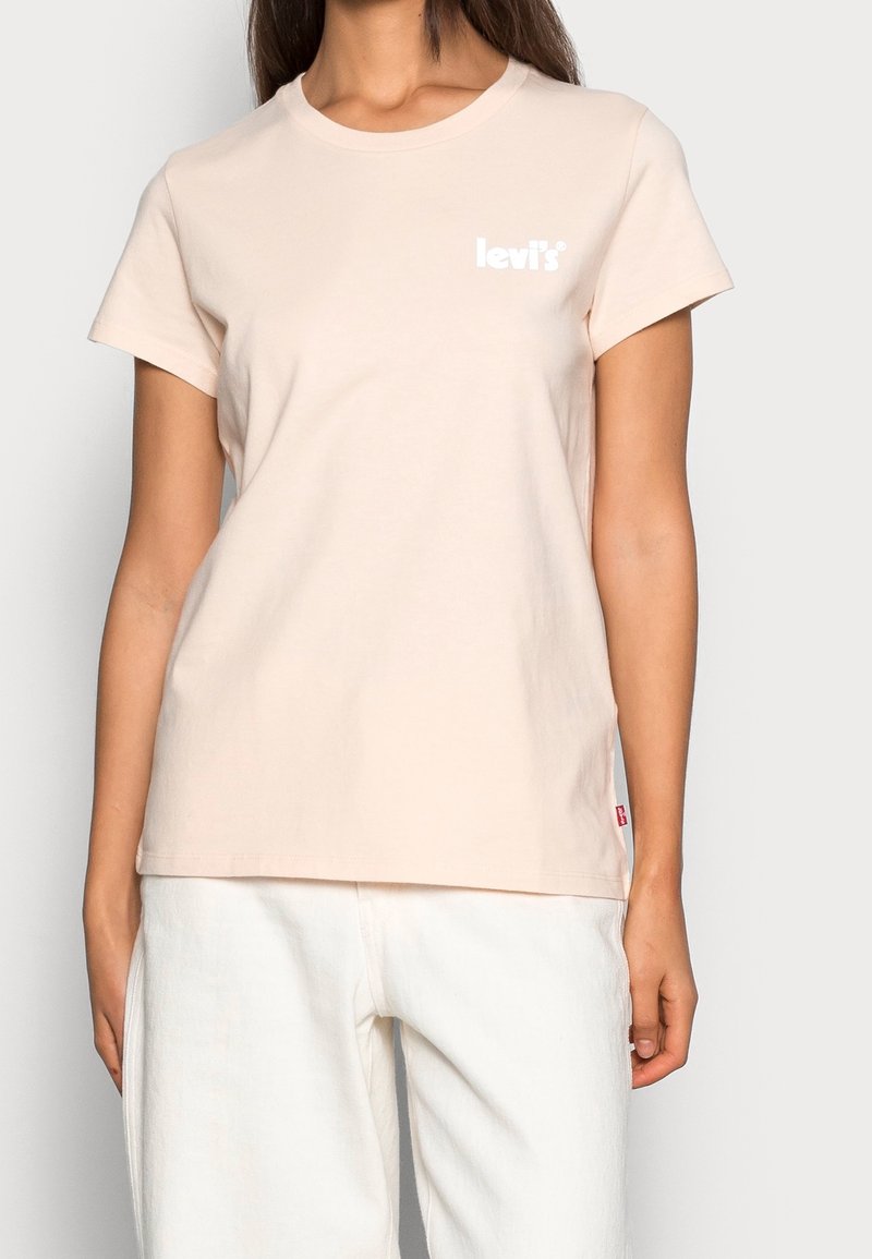 T-shirt en coton rose clair avec un col rond, des manches courtes, et un logo Levi's blanc sur la poitrine. La couture latérale présente une étiquette rouge.