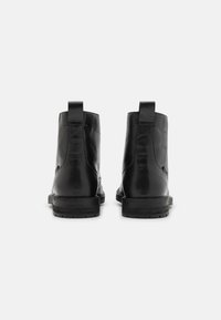 Botas de tobillo de cuero negro con textura suave, punta redonda y bucles para tirar. La suela es de goma con un perfil ligeramente bajo y un patrón de banda de rodadura.