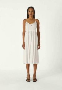 Λευκό μίνι φόρεμα με λεπτές τιράντες, που διαθέτει λεπτομέρειες από eyelet στο μπούστο και μαζεμένη μέση. Λείο ύφασμα, ρομαντική και ρέουσα σιλουέτα.