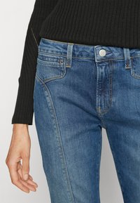 Τζιν παντελόνια σε μεσαίο μπλε λουστράρισμα με ελαφριά φθορά. Ραμμένα στοιχεία, σχέδιο με πέντε τσέπες και ασημένιο κούμπωμα στη μέση.