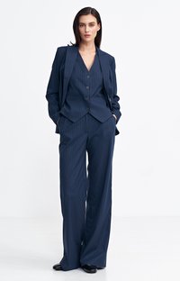 Granatowy garnitur w paski składający się z dopasowanej marynarki z klapami i zapięciem na guziki, w połączeniu z szerokimi spodniami oraz błyszczącymi butami.