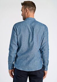 Camicia blu in chambray con colletto alla mandarino, dotata di maniche lunghe, polsini con bottone, una piega posteriore e un tessuto textured.