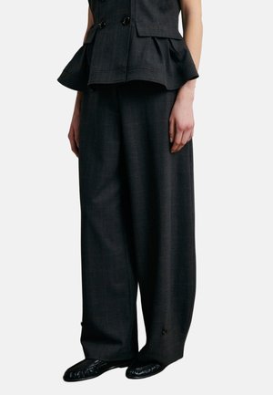 Person iført løstsiddende mørkegrå viddebukser, matchende ærmeløs top med peplum-detalje og sorte flade sko.