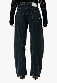 Jeans in denim nero con vestibilità ampia, vita alta, due tasche posteriori e dettagli con orlo a vivo. Etichetta visibile sulla cintura.