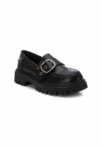 Mocasines de cuero negro con punta redondeada, que presentan una prominente hebilla plateada y una suela de goma gruesa y texturizada con surcos profundos.
